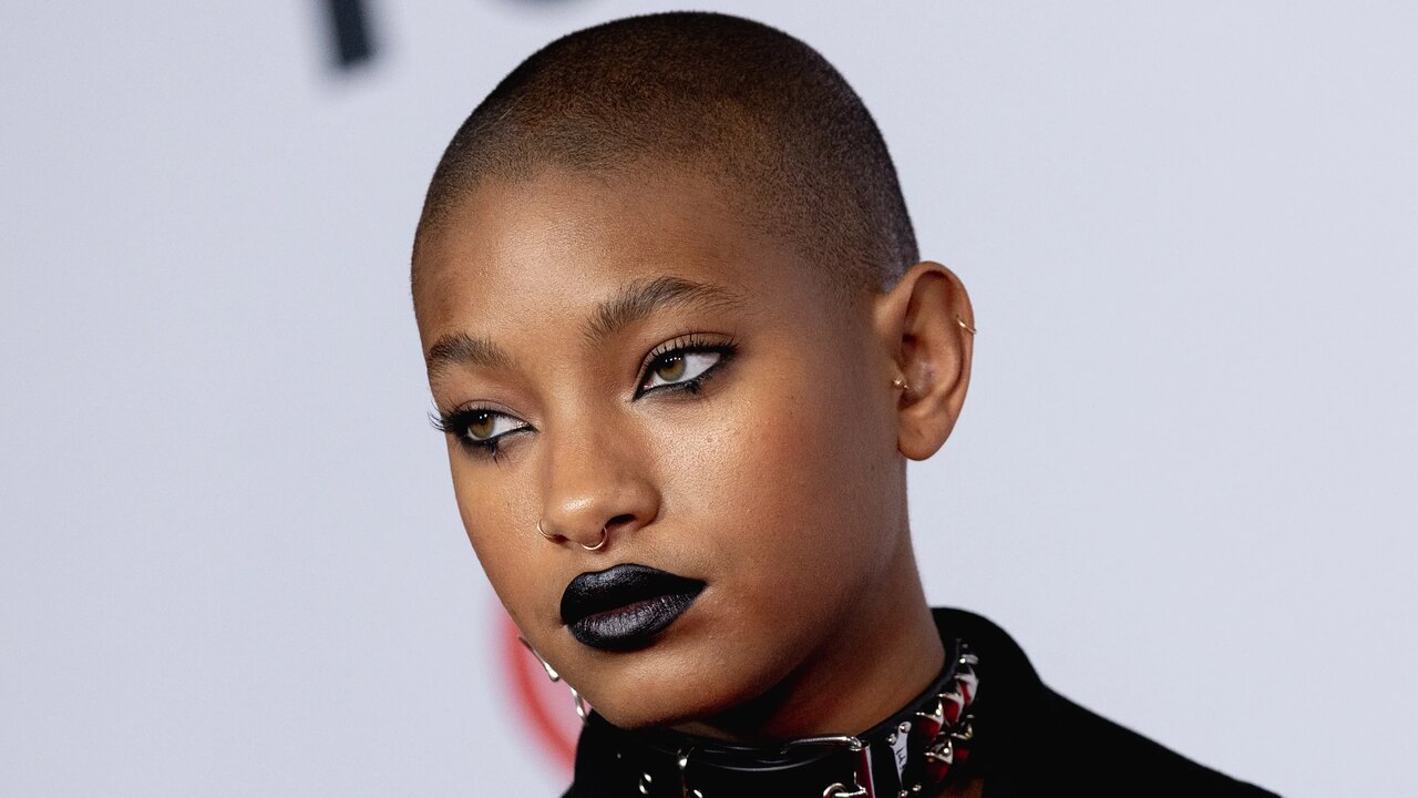 Foto de Willow Smith com jaqueta e batom preto olhando para a direita com ar misterioso